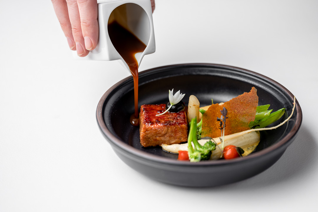 https://hungryformore.be/app/uploads/2024/12/kommilfoo-antwerp-sauce-being-poured-over-a-goat-dish.jpg