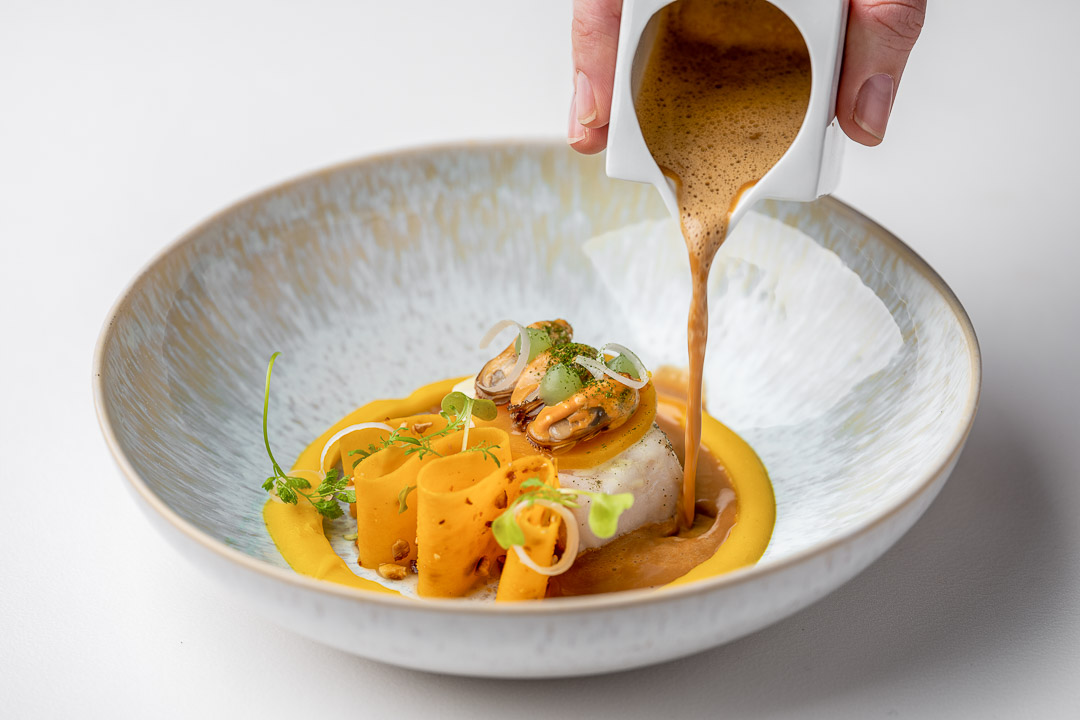 https://hungryformore.be/app/uploads/2024/12/kommilfoo-antwerp-sauce-being-poured-over-mussels-and-plaice.jpg